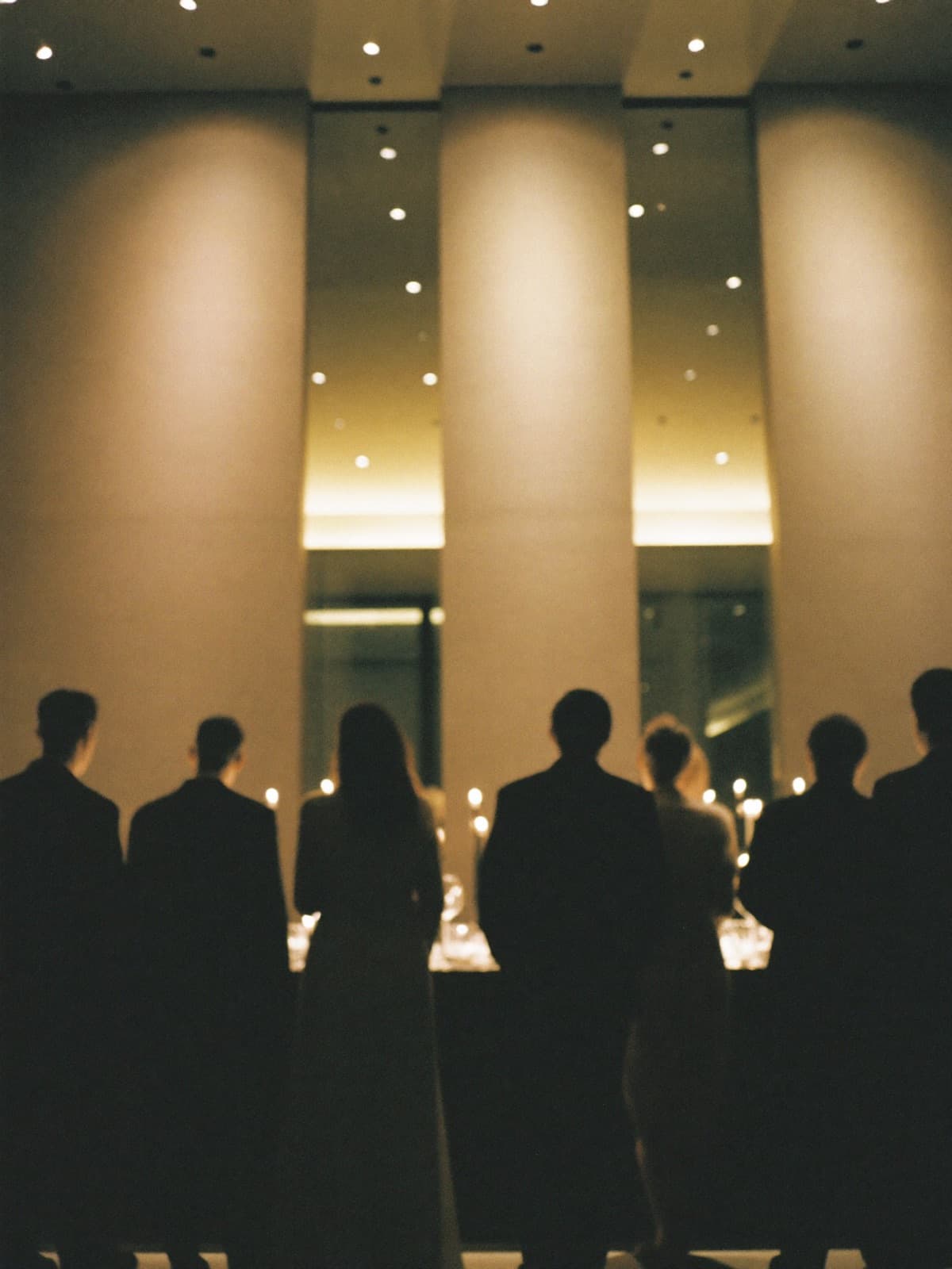 Guests in silhouette at an evening reception, warm gold light on the room behind them
