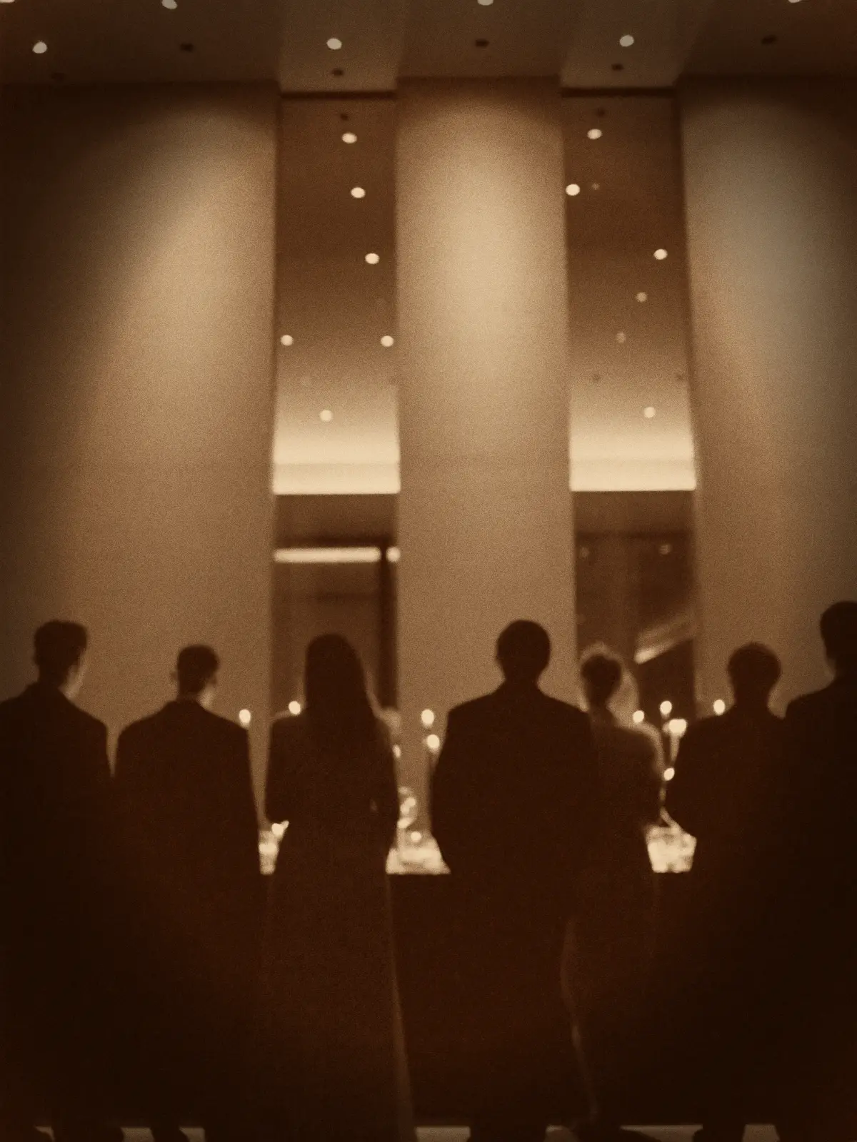 Guests in silhouette at an evening reception, warm gold light on the room behind them